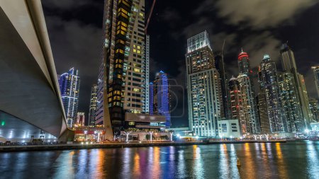 Foto de Dubai Marina paseo marítimo con yates y modernas torres reflejadas en el agua de la noche frente al mar, Emiratos Árabes Unidos. Distrito con canal artificial y rascacielos iluminados alrededor - Imagen libre de derechos