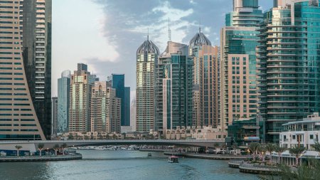 Téléchargez les photos : Dubai Marina waterfront with towers and yachts from bridge in Dubai day to night transition timelapse, Émirats arabes unis. Quartier avec canal artificiel et gratte-ciel illuminé autour - en image libre de droit