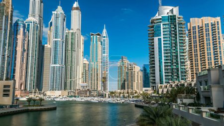 Foto de Dubai Marina paseo marítimo, palmeras, modernas torres con yates flotantes y barcos de puente timelapse, Emiratos Árabes Unidos. Canal artificial y rascacielos alrededor - Imagen libre de derechos