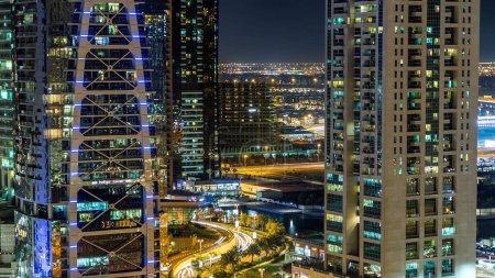 Foto de Edificios de Jumeirah Lakes Towers con tráfico en la carretera noche timelapse aéreo. La vista superior del distrito JLT desde el rascacielos de Dubai Marina - Imagen libre de derechos