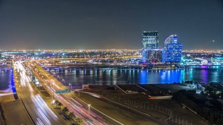 Die Business Bay überquert im Zeitraffer eine 13-spurige Brücke über den Dubai Creek in der Nähe des Flughafens. Reflexion im Wasser in der Nacht