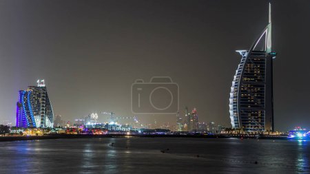 Photo for Dubai skyline with Burj Al Arab hotel at night timelapse. View from kite beach. Dubai marina towers on background. Burj Al Arab is a luxury 5 stars hotel built on an artificial island in front of Jumeirah beach. - Royalty Free Image