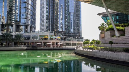 Téléchargez les photos : Vue Timelapse sur les gratte-ciel au bord de l'eau avec palmiers. Bâtiments résidentiels et commerciaux à Jumeirah Lake Towers reflétés dans l'eau à Dubaï, Émirats arabes unis. Vue du front de mer - en image libre de droit