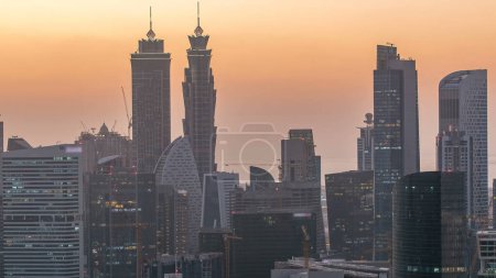 Téléchargez les photos : Vue aérienne d'une grande ville moderne de jour à la nuit transition timelapse avec la circulation et les gratte-ciel éclairés, immeubles de bureaux après le coucher du soleil. Business bay, Dubai, Émirats arabes unis. - en image libre de droit