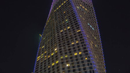 Night close up view from promenade on Dubai Marina modern towers with blinking lights in windows timelapse, United Arab Emirates. Twisted tower look up