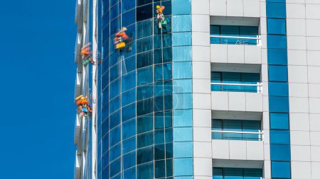Téléchargez les photos : Laveuses lavent les fenêtres du gratte-ciel moderne à Dubaï timelapse, Émirats arabes unis. Vue rapprochée à la journée ensoleillée - en image libre de droit