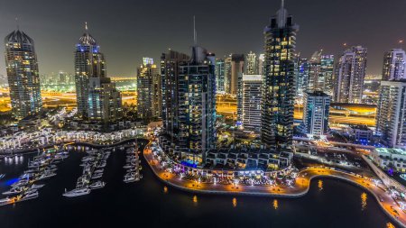 Photo for Aerial top view at night of Dubai Marina promenade and canal with floating yachts and boats in Dubai, UAE. Illuminated modern towers with blinking lights and traffic on the road panoramic view - Royalty Free Image