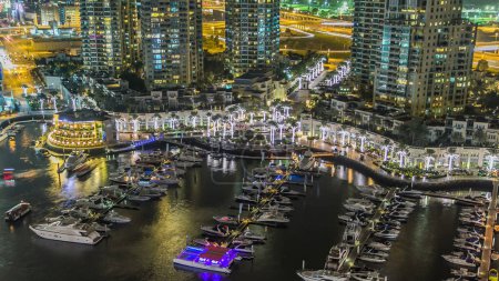 Foto de Vista aérea superior en horario nocturno del paseo marítimo y canal de Dubai Marina con yates flotantes y barcos en Dubai, Emiratos Árabes Unidos. Fuente iluminada con luces parpadeantes y tráfico en la carretera vista panorámica - Imagen libre de derechos