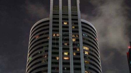 Téléchargez les photos : Regardez vers le haut vue sur les bâtiments modernes dans le quartier des affaires timelapse la nuit. gratte-ciel de façade en verre avec des fenêtres éclatantes. Concept d'économie, finances. Dubai, Émirats arabes unis - en image libre de droit