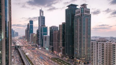 Photo for Downtown Dubai towers day to night transition timelapse. Aerial view of Sheikh Zayed road with skyscrapers after sunset. Traffic on the road and metro line. Beautiful cloudy sky - Royalty Free Image