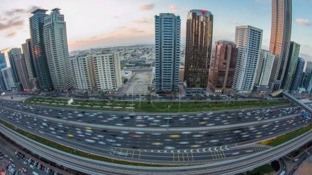 Foto de El centro de Dubái torres de día a noche timelapse transición. Vista aérea de la carretera Sheikh Zayed con rascacielos después de la puesta del sol. Tráfico en la carretera y la línea de metro. Hermoso cielo nublado. Panorama de lentes Fisheye - Imagen libre de derechos