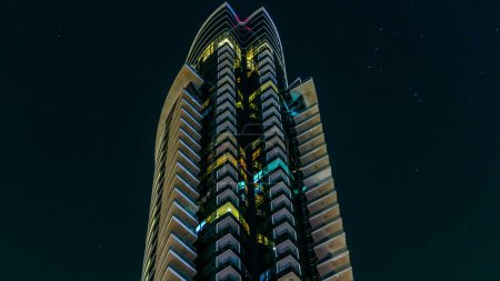 Photo for Look up view of modern buildings in business district timelapse by night. Glass facade skyscrapers with glowing windows. Concept of economics, finances. Dubai, UAE - Royalty Free Image