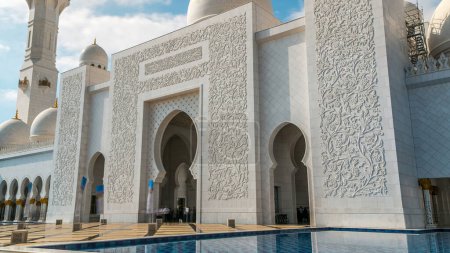 Photo for Pool with water near entrance to Sheikh Zayed Grand Mosque timelapse located in Abu Dhabi - capital city of United Arab Emirates. It is largest mosque in UAE. Blue cloudy sky - Royalty Free Image