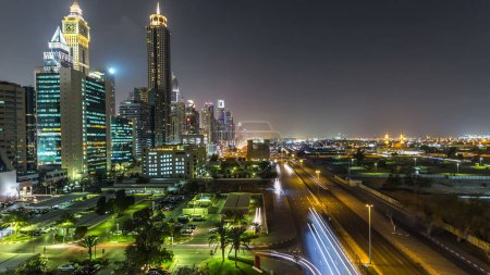 Photo for Downtown Dubai towers night timelapse. Aerial view of Sheikh Zayed road with skyscrapers. Traffic on the road and cars on parking. Blinking lights and trails - Royalty Free Image