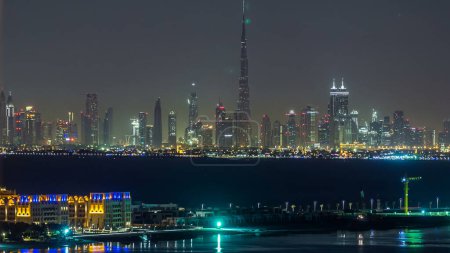 Foto de Skyline del centro de Dubai por la noche timelapse. Panorama de rascacielos modernos de ciudad construidos en el desierto. Vista aérea superior desde la palmera jumeirah con reflejo en el agua - Imagen libre de derechos