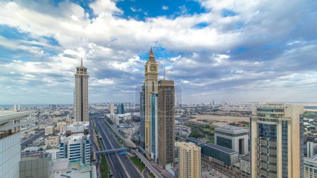 Photo for Dubai skyscrapers timelapse evening sunset time. Dubai Metro station and traffic on Sheikh Zayed Road. Aerial top view from tower rooftop. Beautiful cloudy sky - Royalty Free Image