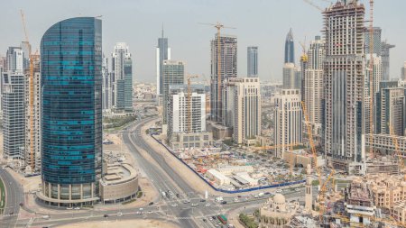 Téléchargez les photos : Downtown Dubai et la baie d'affaires skyline avec des tours résidentielles et de bureaux timelapse, vue depuis le toit. Ciel nuageux et circulation sur une route - en image libre de droit