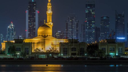 Téléchargez les photos : Moderne ville de Dubaï horizon timelapse avec Rashid Al Hadeeth Mosquée la nuit avec des gratte-ciel éclairés sur la surface de l'eau. Vue de l'île de Daria au centre-ville de Dubaï - en image libre de droit