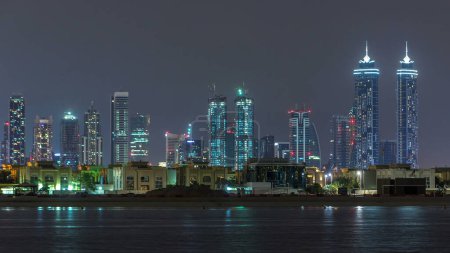Photo for Modern Dubai city skyline timelapse at night with illuminated skyscrapers and hotels over water surface. View from Daria island to Dubai downtown and business bay - Royalty Free Image
