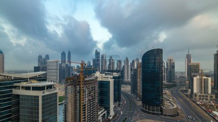 Foto de Dubai torres de la bahía de negocios temprano en la mañana timelapse aéreo. Vista de la azotea de algunos rascacielos y nuevas torres en construcción. Nubes coloridas en el cielo - Imagen libre de derechos