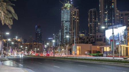 Téléchargez les photos : Street view of Dubai skyline timelapse and rush hour traffic in downtown in night. Route avec palmiers et tours modernes sur fond - en image libre de droit