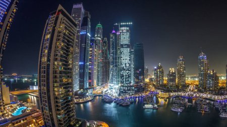 Téléchargez les photos : Dubai Marina la nuit timelapse, lumières scintillantes et gratte-ciel les plus hauts lors d'une soirée claire. Tours éclairées, yachts et circulation sur la route en arrière-plan - en image libre de droit