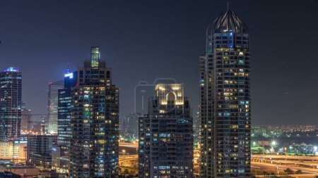 Téléchargez les photos : Dubai Marina la nuit timelapse, lumières scintillantes dans les fenêtres et les gratte-ciel les plus hauts. Tours éclairées et circulation sur la route en arrière-plan - en image libre de droit