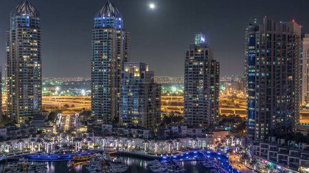 Téléchargez les photos : Dubai Marina la nuit timelapse, lumières scintillantes et gratte-ciel les plus hauts. Tours éclairées et circulation sur la route en arrière-plan. Lune montante sur le ciel - en image libre de droit