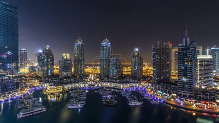 Photo for Dubai Marina during all night timelapse, Glittering lights switching off and tallest skyscrapers. Illuminated towers, yachts and traffic on the road on background - Royalty Free Image