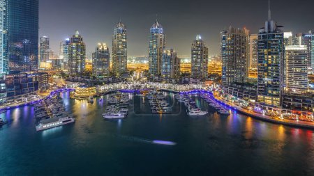 Dubai Marina por la noche timelapse, luces brillantes y rascacielos más altos durante una noche clara. Torres iluminadas, yates y el tráfico en la carretera en el fondo
