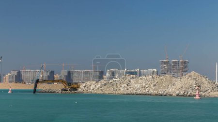 Téléchargez les photos : Pelle construisant une nouvelle pièce sur le timelapse Palm Jumeirah. Construction du terminal portuaire. Skyline Dubaï sur fond - en image libre de droit