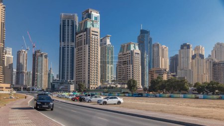 Téléchargez les photos : Vue panoramique sur Dubai Marina et les gratte-ciel JBR avec des voitures timelapse, Skyline, Vue de la mer, Émirats arabes unis. Ciel bleu à une journée ensoleillée et circulation sur la route - en image libre de droit