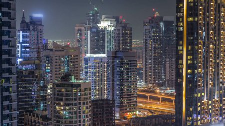 Foto de Dubai Marina y Jumeirah Lakes Towers en horario nocturno, luces brillantes y rascacielos más altos. Torres iluminadas con luz en las ventanas y tráfico en la carretera en el fondo - Imagen libre de derechos