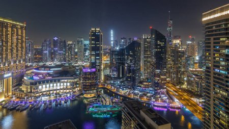 Foto de Iluminación nocturna del timelapse panorámico aéreo Dubai Marina, Emiratos Árabes Unidos. Rascacielos modernos y edificios residenciales. Tráfico en la carretera. Yates y barcos cerca del centro comercial en la ciudad del canal artificial - Imagen libre de derechos