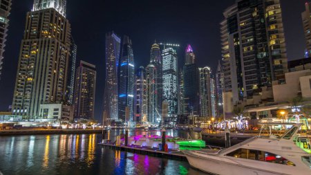 Foto de Bahía marina de Dubai con yates y barcos timelapse hiperlapso. Rascacielos más altos iluminados por la noche reflejados en el agua del canal - Imagen libre de derechos