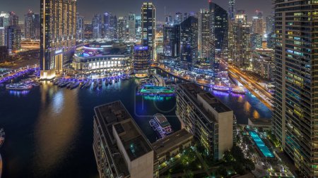 Photo for Night illumination of Dubai Marina aerial timelapse, UAE. Modern skyscrapers and residential buildings. Traffic on the road. Yachts and boats near shopping mall on artificial canal city - Royalty Free Image
