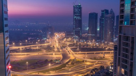 Téléchargez les photos : Vue aérienne d'une intersection de la route et des tours modernes dans une grande ville nuit à jour passage timelapse. Paysage urbain du quartier Marina de Dubaï aux EAU avec voitures et gratte-ciel
. - en image libre de droit
