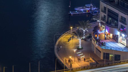 Téléchargez les photos : Promenade et canal à Dubai Marina avec des yachts autour de la nuit timelapse, Émirats arabes unis. Vue aérienne avec restaurants et cafés sur la passerelle - en image libre de droit