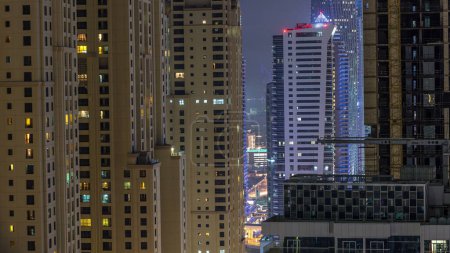 Téléchargez les photos : Illumination nocturne de Dubai Marina et JBR aerial timelapse, EAU. gratte-ciel et bâtiments résidentiels modernes. Circulation sur la route et lumière vive dans les fenêtres - en image libre de droit