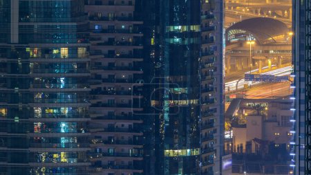 Téléchargez les photos : Tours résidentielles avec éclairage et éclairage timelapse. Station de métro et promenade sur Dubai Marina skyline la nuit. Trafic près des gratte-ciel avec des fenêtres éclatantes - en image libre de droit