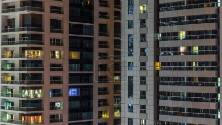 Foto de Ventanas brillantes de rascacielos al atardecer. Vista de los modernos edificios residenciales de gran altura en el puerto deportivo de Dubai. Gente moviéndose dentro de apartamentos. Vista superior aérea - Imagen libre de derechos