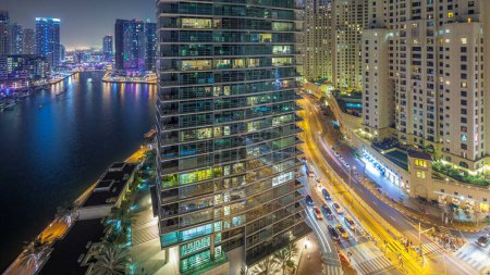 Foto de Iluminación nocturna de Dubai Marina y JBR timelapse aéreo, Emiratos Árabes Unidos. Rascacielos modernos y edificios residenciales. Tráfico en la carretera y ventanas brillantes - Imagen libre de derechos