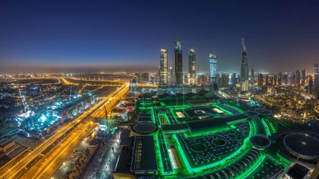 Dubai downtown night to day transition timelapse with modern skyscrapers, mall and traffic on the road before sunrise. Top panoramic view from above