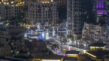 Foto de Dubai céntrico timelapse noche con modernos rascacielos iluminados, plaza con palmeras y el tráfico en la carretera. Vista superior desde arriba - Imagen libre de derechos