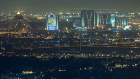 Foto de Vista aérea al distrito de Deira con aeropuerto en el timelapse de fondo y edificios iluminados. Vista superior desde el centro de Dubai. Tráfico en la carretera. Dubai, Emiratos Árabes Unidos - Imagen libre de derechos