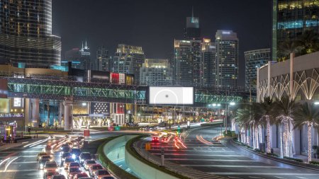 La circulation automobile sur la route achalandée près du centre commercial la nuit dans le centre-ville timelapse. Gratte-ciel avec éclairage nocturne. Vue de dessus depuis le pont. Dubai, Émirats arabes unis