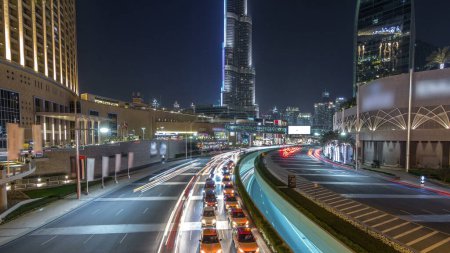 Foto de Tráfico de coches en carretera cerca del centro comercial por la noche en el centro de hiperlapso timelapse. Rascacielos con iluminación nocturna. Vista superior desde el puente. Dubai, Emiratos Árabes Unidos - Imagen libre de derechos
