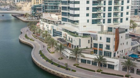Téléchargez les photos : Promenade et canal à Dubai Marina avec des gratte-ciel de luxe et des yachts autour de timelapse, Émirats arabes unis. Vue aérienne du dessus du front de mer avec palmiers - en image libre de droit