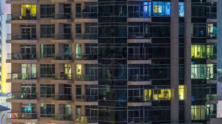 Foto de Ventanas brillantes de rascacielos por la noche timelapse. Vista de los modernos edificios residenciales de gran altura en el puerto deportivo de Dubai. Gente moviéndose adentro. Vista superior aérea
. - Imagen libre de derechos