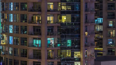Foto de Ventanas del edificio de varios pisos de iluminación de vidrio y acero en el interior y personas en movimiento dentro de timelapse. Vista aérea de los modernos rascacielos residenciales en Dubai marina
. - Imagen libre de derechos